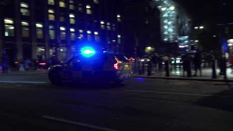 A-Metropolitan-police-car-drives-across-Westminster-Bridge-at-night-with-blues-lights-flashing-and-turns-right-on-to-Embankment-by-Portcullis-House