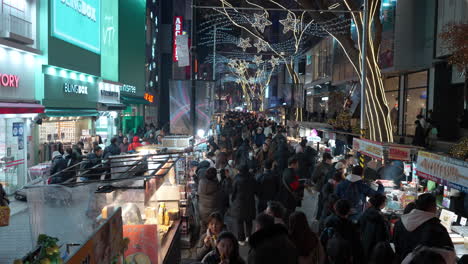 Multitud-De-Personas-Comiendo-Comida-Callejera-En-El-Mercado-Nocturno-De-Myeongdong-En-Invierno,-Puestos-Minoristas---ángulo-Alto