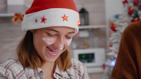 Portrait-of-granddaughter-with-flour-on-face-wearing-santa-hat-cooking-delicious-dessert