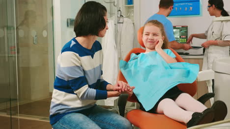 Sad-child-showing-affected-mass-to-her-mother-sitting-in-stomatological-chair