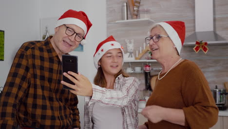 Happy-family-wearing-santa-hat-enjoying-winter-season-together-discussing-with-remote-friends