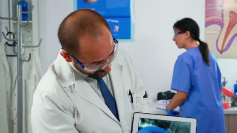 Doctor-holding-tablet-with-jaw-x-ray-showing-it-to-patient
