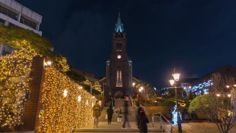 Lapso-Nocturno-De-La-Catedral-De-Myeongdong---Gente-Subiendo-Y-Bajando-Escalones-En-El-Parque-Decorado-Con-Guirnaldas-Brillantes-Para-La-Temporada-Navideña---Acercar