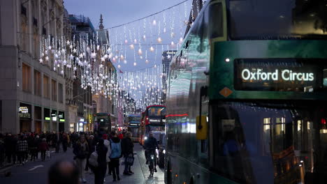 Un-Autobús-Verde-Número-55-De-Oxford-Circus-Se-Aleja-Mientras-Los-Compradores-Navideños-Llenan-Las-Aceras-Bajo-Las-Luces-Festivas-En-Oxford-Street-Al-Atardecer