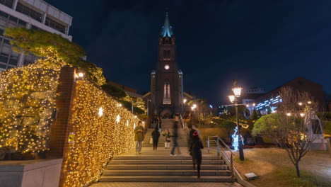 People-Walking-on-Steps-of-Myeongdong-Cathedral-at-Night-Taking-Pictures-With-Shiny-Garlands-Decorations---Time-Lapse-in-Seoul,-South-Korea