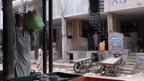 Old-men-dressed-in-white-worker-carry-produce-in-from-of-market-in-Karachi,-Pakistan