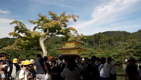 An-Einem-Sonnigen-Tag-Sieht-Man-Geschäftige-Menschenmengen-Mit-Kinkakuji-Im-Hintergrund-Vorbeigehen