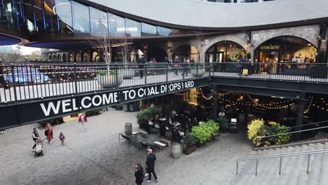 Overlooking-Signage-Saying-Welcome-To-Coal-Drops-Yard-With-Shoppers-Walking-Past