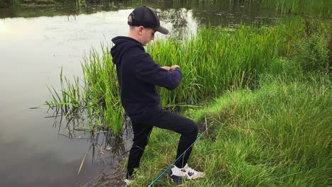 Un-Joven-Al-Lado-De-Un-Lago-De-Pesca-Pone-Cebo-En-El-Anzuelo-De-La-Línea-De-Pesca