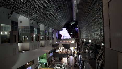 Kyoto-modern-architectural-train-station-at-night-time,-pedestrians-moving-towards-platforms