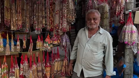 Wide-shot,-a-shopkeeper-on-Street-Road-is-selling-temple-utensils-and-flower-garlands