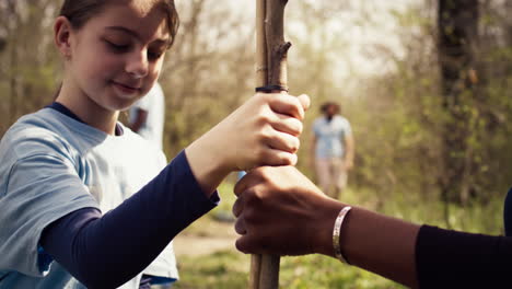 Child-and-her-friend-are-planting-a-small-tree-in-the-woods