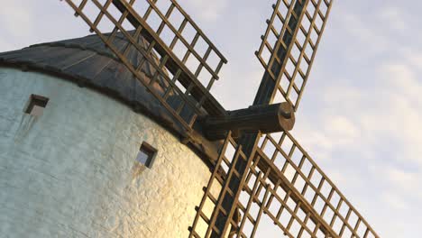 Vintage-agriculture-windmill’s-wings-working-and-rotating-slowly-during-sunset-with-clouds-in-the-background.-Camera-slowly-pans-around-a-building.-Spinning-turbine,-old-technology,-an-energy-exchange