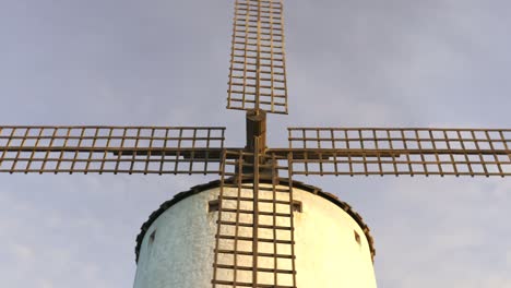 Vintage-agriculture-windmill’s-wings-working-and-rotating-slowly-during-sunset-with-clouds-in-the-background.-Camera-slowly-pans-around-a-building.-Spinning-turbine,-old-technology,-an-energy-exchange