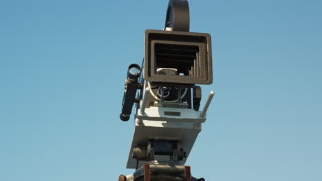 Old,-retro-vintage-film-camera-with-a-clear-blue-sky-in-the-background.-Sunlight-illuminates-a-reel-case-shoving-hollywoods-cinematographic-equipment.-Camera-tracks-back-from-the-equipment.