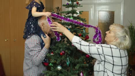 Girl-kid-with-senior-grandma,-grandpa-decorating-artificial-Christmas-tree-with-ornaments-and-toys