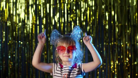 Stylish-teenager-kid-girl-standing-on-backlit-blue-neon-lights-and-points-at-blank-space,-agree-sign