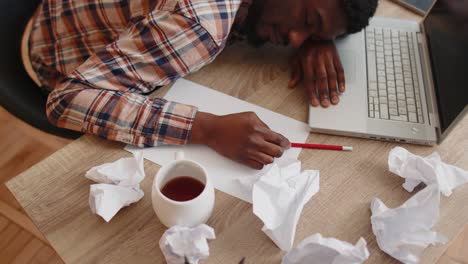 Tired-man-at-home-office-falling-asleep-on-table-with-laptop-computer,-crumpled-sheets-of-paper