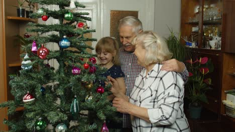 Children-girl-with-elderly-couple-grandparents-decorating-artificial-Christmas-pine-tree-at-home