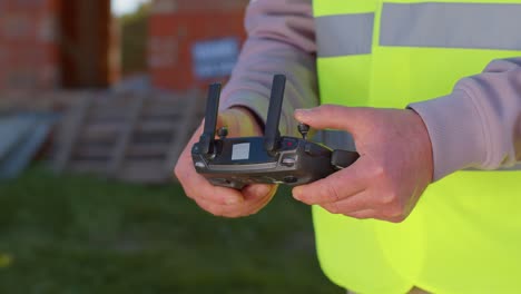 Operador-De-Drones-Que-Sostiene-Un-Control-Remoto-Controla-Un-Avión-Frente-Al-Sitio-De-Construcción