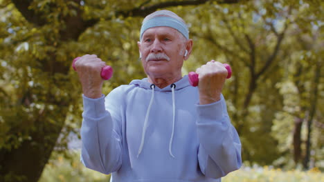 Hombre-Mayor-Haciendo-Ejercicio,-Haciendo-Ejercicios-De-Levantamiento-De-Pesas-Con-Mancuernas,-Practicando-Entrenamiento-Deportivo-En-El-Parque