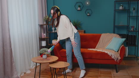 Young-dancing-woman-dusting-furniture-alone-caring-for-hygiene-using-colorful-duster-in-room-at-home