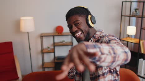 Un-Joven-Muy-Alegre-Con-Auriculares-Inalámbricos-Bailando,-Cantando-En-Un-Acogedor-Sofá-En-La-Sala-De-Estar-De-Casa