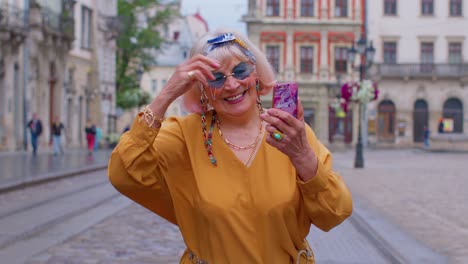 Elderly-grandmother-woman-tourist-with-smartphone,-smiling,-listening-music-in-app-wearing-earphones