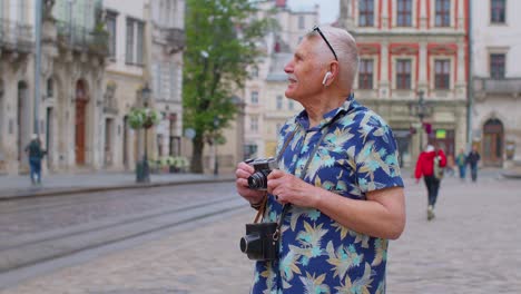 Älterer-Tourist-Mit-Retro-Fotokamera,-Der-über-Kopfhörer-Musik-Hört-Und-Im-Freien-Tanzt-Und-Spaß-Hat