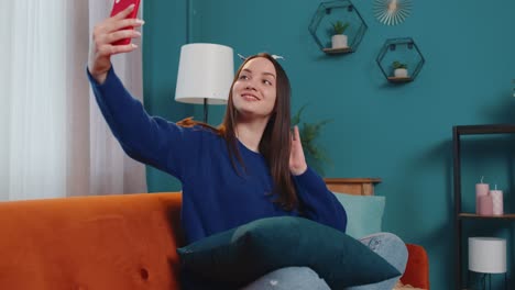 Woman-on-sofa-at-home-with-smartphone-taking-selfie-on-mobile-phone-cam,-virtual-video-call-online