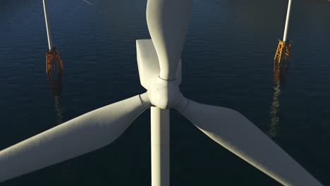 An-offshore-Windmill-farm-in-the-water.-Multiple-wind-turbines-producing-electric-power-using-the-environmental-force-of-wind-with-beautiful-mountains-in-the-background,-and-wavy-water-beneath-them.