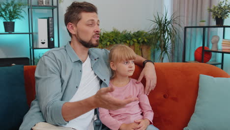 Young-man-father-having-trustworthy-conversation,-talking-with-daughter-child-kid-at-home-sofa