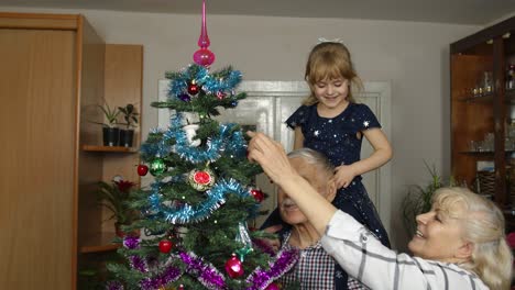 Kid-girl-with-senior-grandmother-and-grandfather-decorating-artificial-Christmas-tree-with-toys