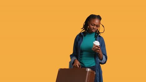 Tired-girl-travelling-with-suitcase,-drinking-coffee,-studio-background