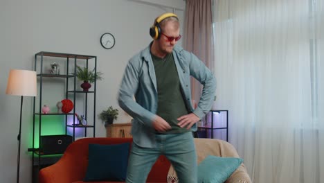 Un-Joven-Muy-Alegre-Con-Auriculares-Inalámbricos-Bailando,-Cantando-En-Un-Acogedor-Sofá-En-La-Sala-De-Estar-De-Casa