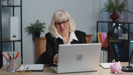 Irritated-senior-business-woman-hits-table-with-fist,-closes-broken-laggy-buggy-laptop-computer