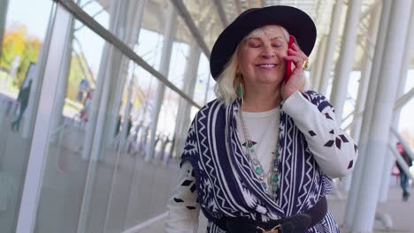 Senior-tourist-grandmother-woman-walking-on-international-airport-hall,-using-mobile-phone,-talking