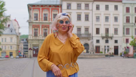 Senior-old-tourist-woman-in-stylish-clothes-talking-on-mobile-phone-while-walking-on-city-street