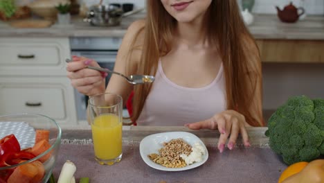 Lovely-girl-eating-raw-sprouts-buckwheat-with-nuts-in-kitchen-with-fresh-vegetables-and-fruits