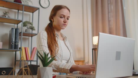 Young-woman-girl-using-laptop-computer-sitting-at-table-working,-typing-on-keyboard-from-home-office