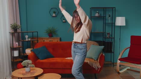 Overjoyed-young-woman-in-wireless-headphones-dancing,-singing-on-cozy-couch-in-living-room-at-home