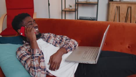 Young-man-using-laptop-computer-sitting-on-sofa-working,-online-shopping-from-home-office