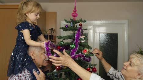 Kleines-Mädchen-Mit-Großmutter-Und-Großvater,-Die-Einen-Künstlichen-Weihnachtsbaum-Mit-Spielzeug-Dekorieren