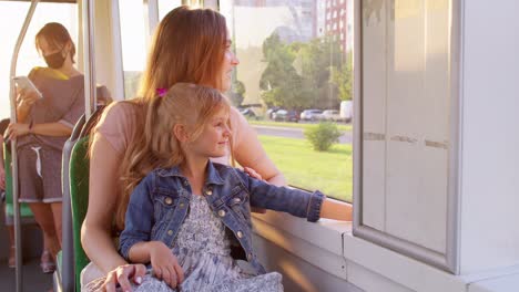 Family-rides-in-public-transport,-woman-with-little-child-girl-sit-together-and-look-out-window-tram