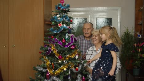 Abuelo,-Abuela-Y-Nieta-Mayores-Encienden-Guirnaldas-En-Un-árbol-De-Navidad-Artificial