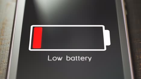 Smartphone-Bildschirm-Mit-Benachrichtigung-über-Niedrigen-Batteriestatus.-Eine-Warnmeldung-Mit-Blinkendem-Batteriesymbol-über-Niedrige-Batterieleistung-Oder-Erschöpfung.-Nahaufnahme-Eines-Generischen-Smartphones-Auf-Einem-Holzschreibtisch.