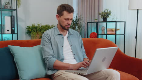 Young-man-freelancer-sitting-on-sofa-closing-laptop-pc-after-finishing-work-in-living-room-at-home