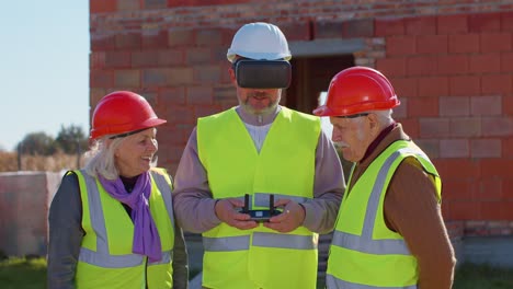 Trabajador-Especializado-Vuela-En-Drone-En-El-Sitio-De-Construcción,-Mostrando-La-Casa-A-Los-Clientes-De-Los-Abuelos