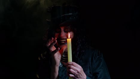 Frightening-creepy-senior-woman-with-Halloween-witch-makeup-looking-at-candle,-conjure,-hex,-wiz