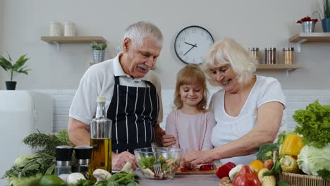 Pareja-Mayor,-Abuela-Y-Abuelo-En-La-Cocina-Alimentando-A-Su-Nieta-Con-Pimienta-Picada